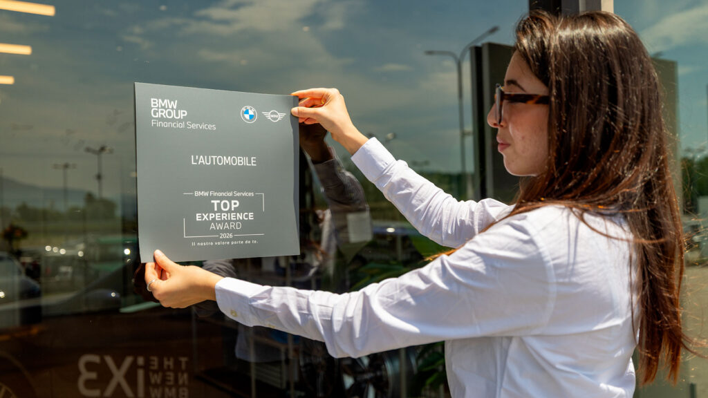 Vediamo una ragazza che applica la targa adesiva del Top Experience Award 2026 alla vetrina del Partner